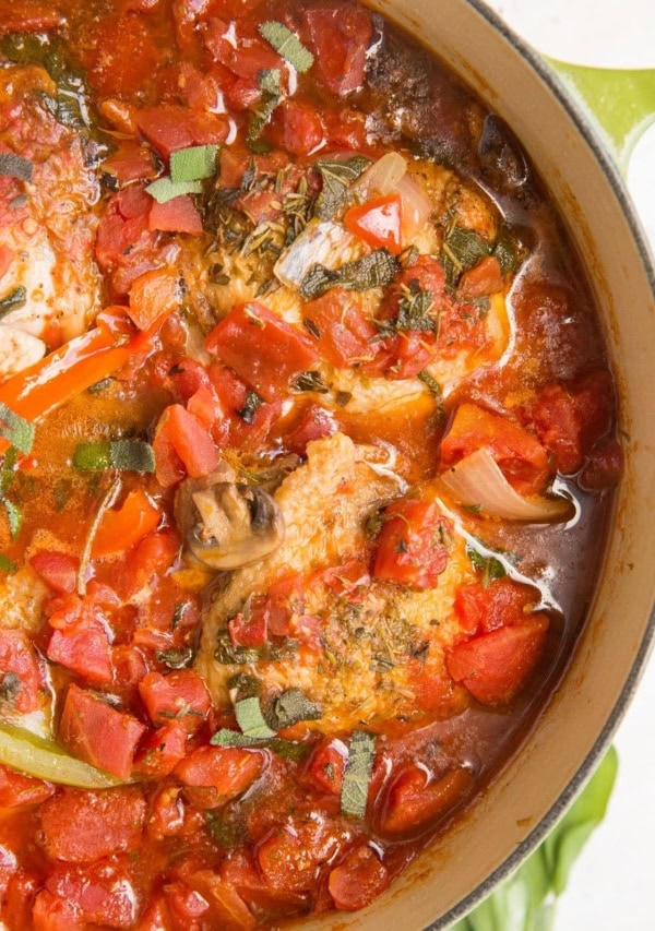 Dutch oven full of chicken cacciatore with tomato sauce, fresh herbs, and vegetables