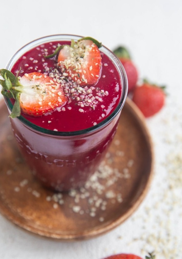 Glass of anti-inflammatory beet smoothie with a beautiful red color. The smoothie is sprinkled with hemp seeds and has a sliced strawberry on top.