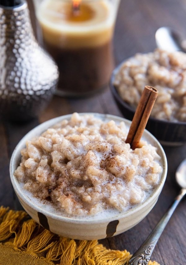 Two bowls of dairy-free rice pudding with a candle in the background and a spoon and golden napkin to the side.