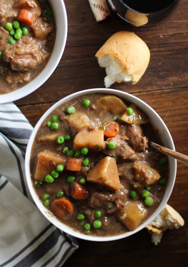 Top down photograph of white bowl of beef stew on a dark rustic wood background