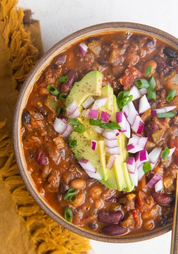 Top down bowl of turkey chili with sliced avocado, green onions and red onions on top