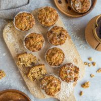Top down photo of a cutting board of paleo morning glory muffins as well as two wooden plates with muffins on them, ready to eat.