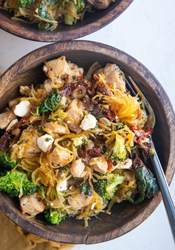 Top down photo of two wooden bowls of chicken spaghetti squash with a golden napkin to the side.