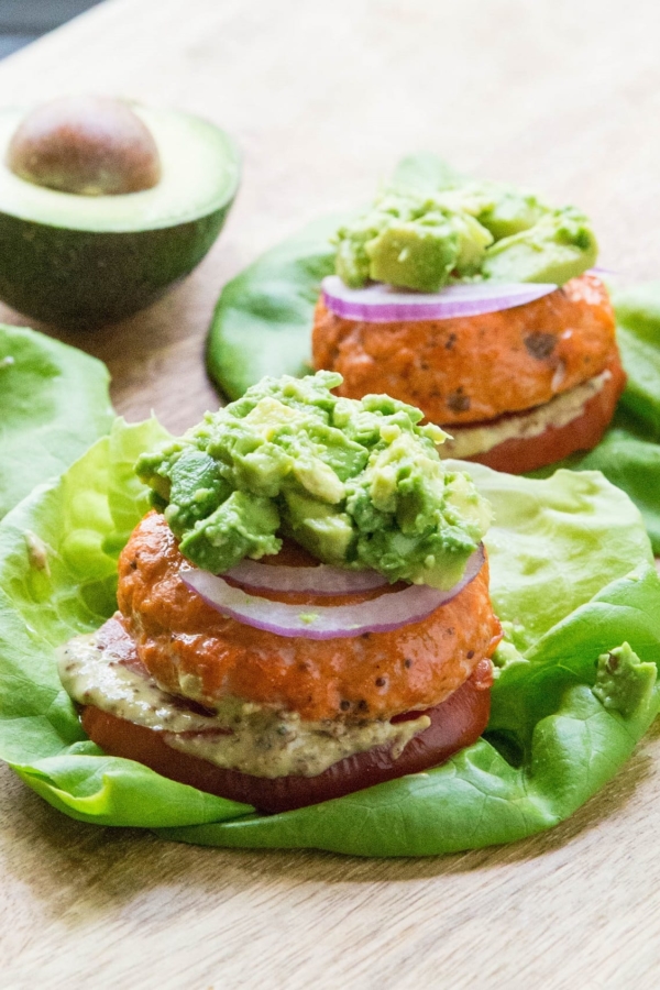 Baked Salmon burgers with mashed avocado on top, red onion, tomato and mustard on a lettuce bun
