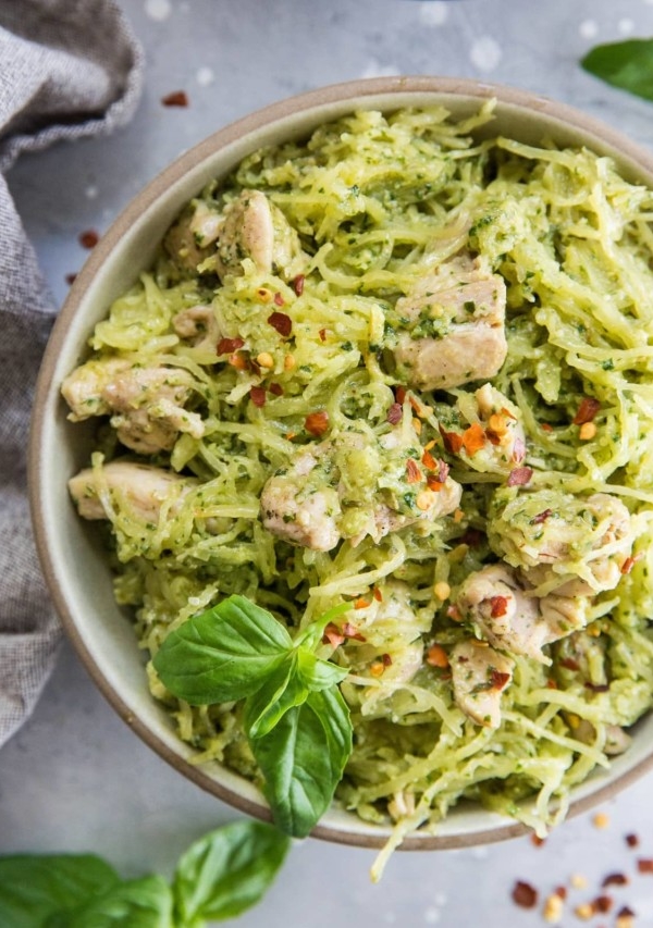 Close up top down image of two bowls of chicken pesto spaghetti squash with basil leaves and red pepper flakes for garnish.