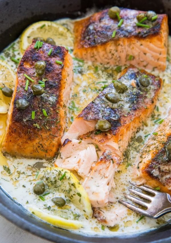 Cast iron skillet with cooked crispy salmon and a creamy dill sauce inside.