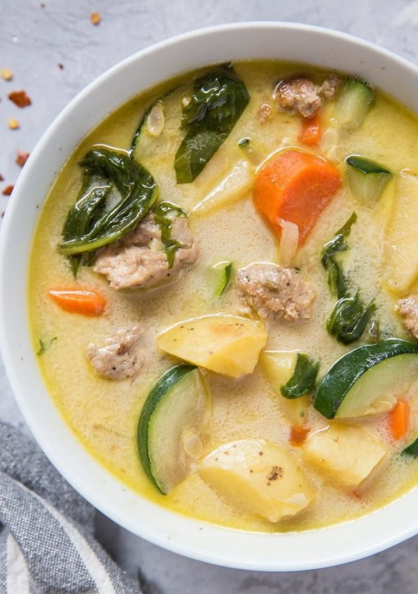 Top down photo of a big bowl of hearty ground turkey soup with grey striped napkin and fresh garlic to the side