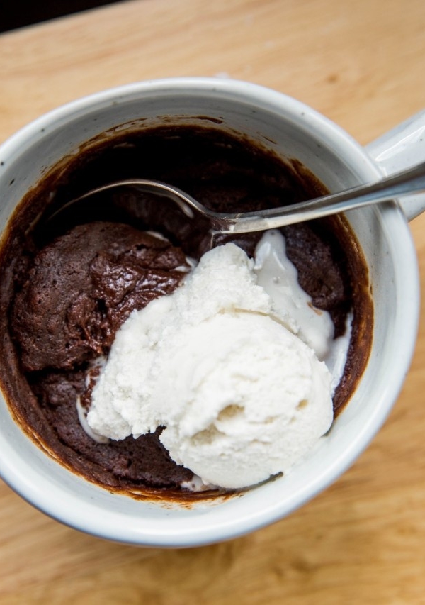 Top down close up photo of a mug brownie with a small scoop of vanilla ice cream on top.