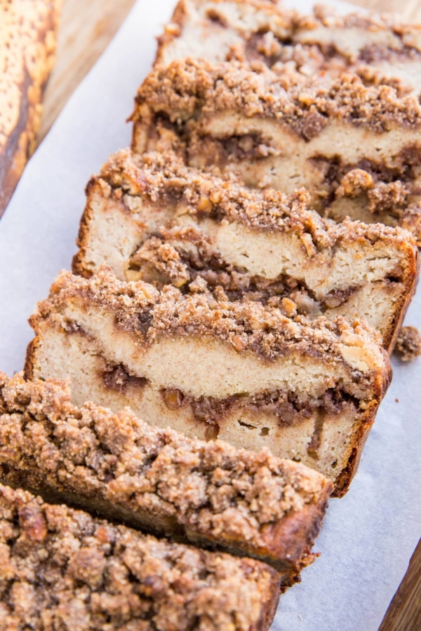 Loaf of Paleo Cinnamon Swirl Banana Bread cut into slices on a wood cutting board. Grain-Free, dairy-free, refined sugar-free healthy banana bread with streusel topping. Delicious gluten-free recipe for breakfast or snack.