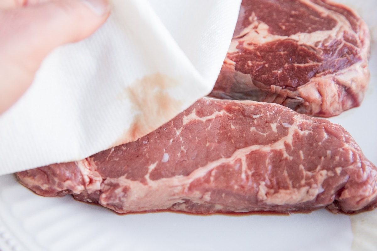 Steaks on a plate being pat dry with a paper towel