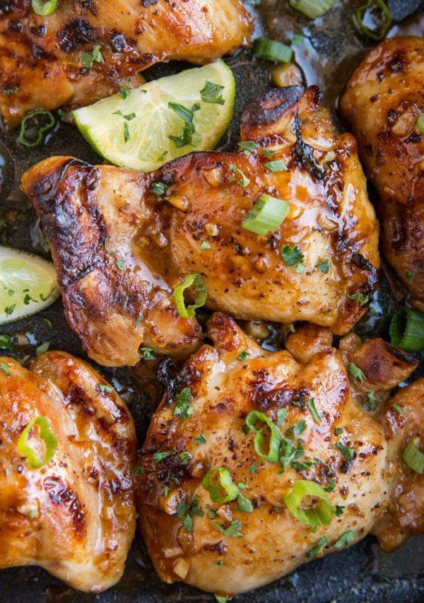 Close up image of Asian Boneless Baked Chicken Thighs with green onion sprinkled on top and some limes