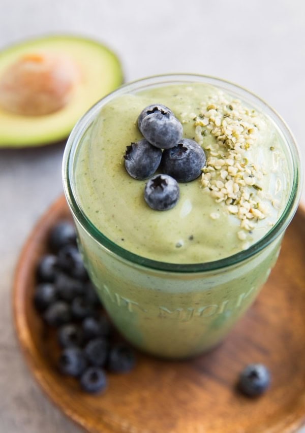 Green avocado smoothie in a glass with blueberries and hemp seeds on top