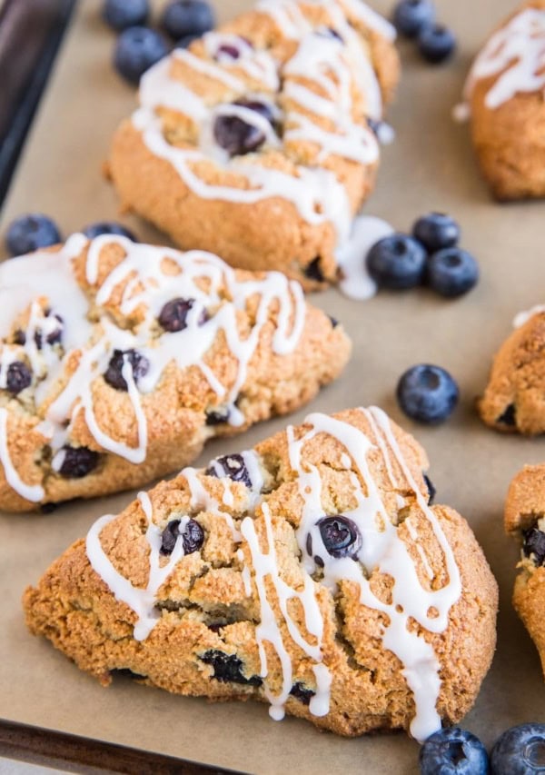 Baking sheet of blueberry almond flour scones with fresh blueberries and a glaze