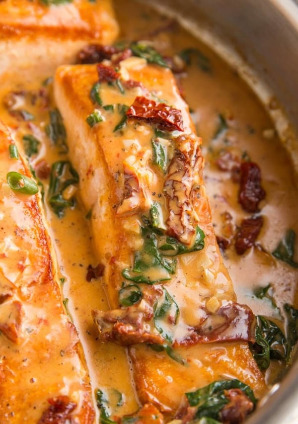 Salmon filets in a skillet with sun-dried tomato sauce.