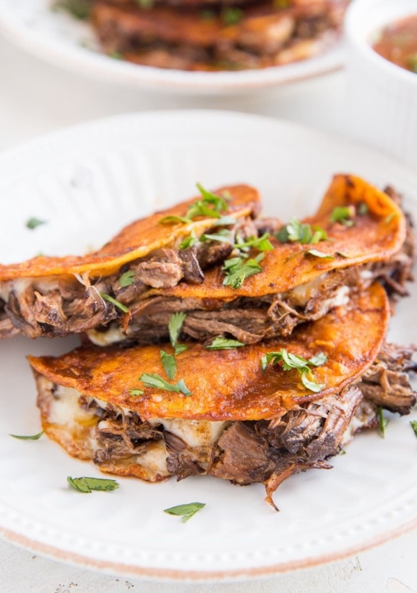 Two plates of birria tacos sprinkled with cilantro