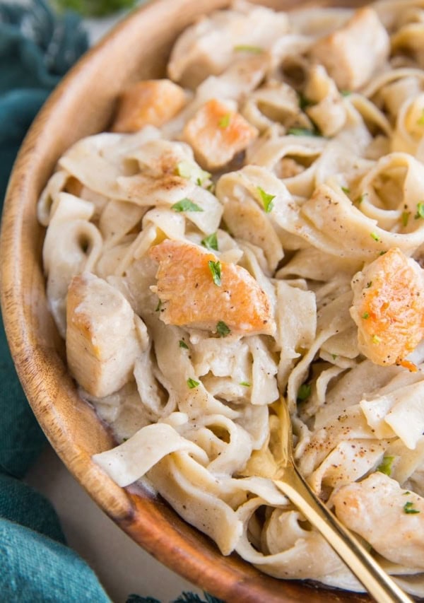 Close up image of creamy chicken fettuccine alfredo in a wooden bowl with a blue napkin and a gold fork