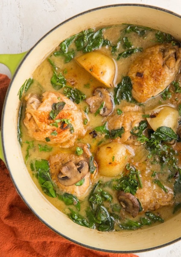 Top down photo of a green Dutch oven full of chicken and potatoes with a red napkin to the side