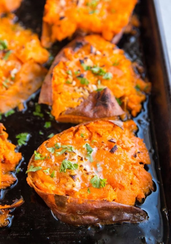 Sheet pan of smashed sweet potatoes with butter on top, garnished with fresh parsley