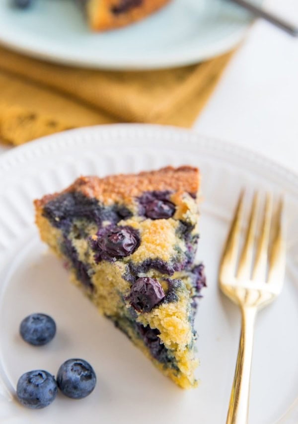 Two slices of keto blueberry cake on plates with fresh blueberries to the side and forks