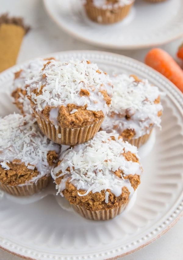 Keto Carrot Cake Muffins sitting on a plate with carrots in the background and another plate of muffins