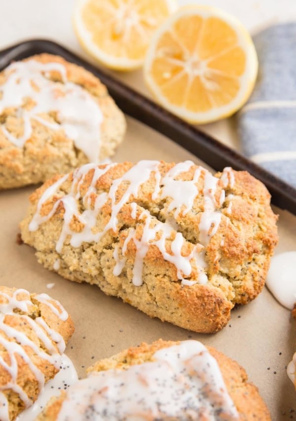 Lemon poppy seed scones on a baking sheet with lemons in the background