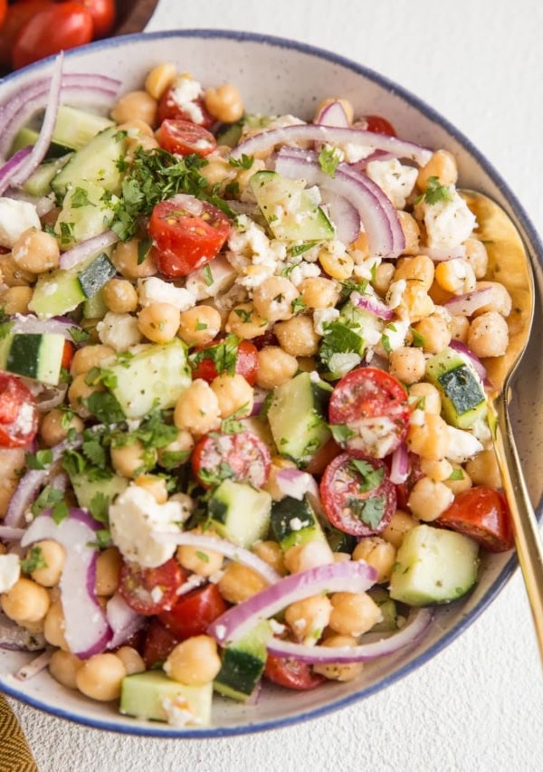 Angle shot of chickpea salad in a bowl with a gold spoon and a wooden bowl of tomatoes