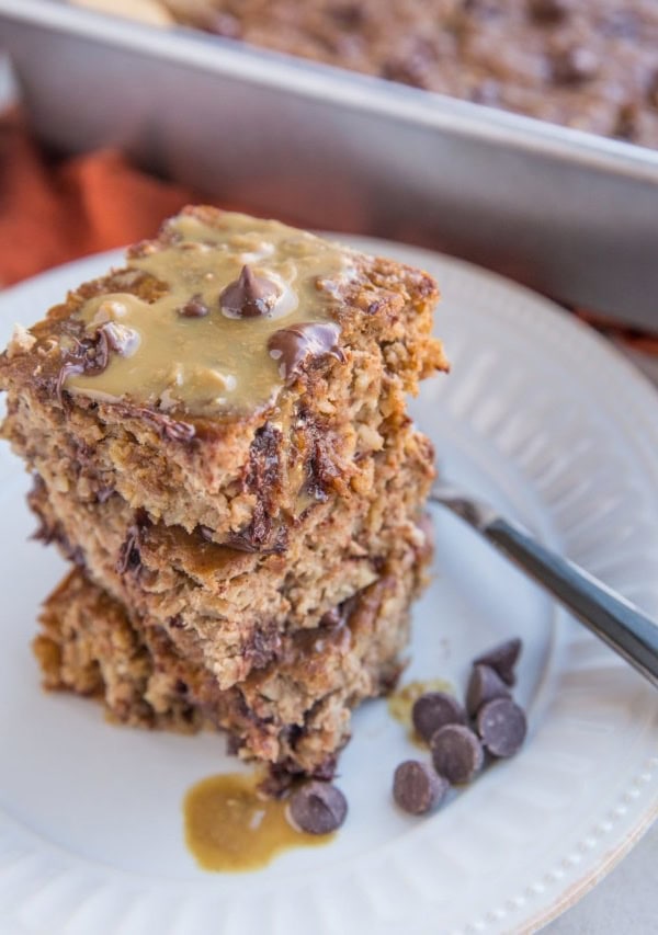 Banana Peanut Butter Baked Oatmeal stacked on a plate with the baking dish in the background