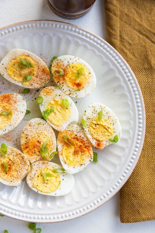 Hard boiled eggs sliced in half and sprinkled with salt, pepper, and paprika and green onions on a white plate