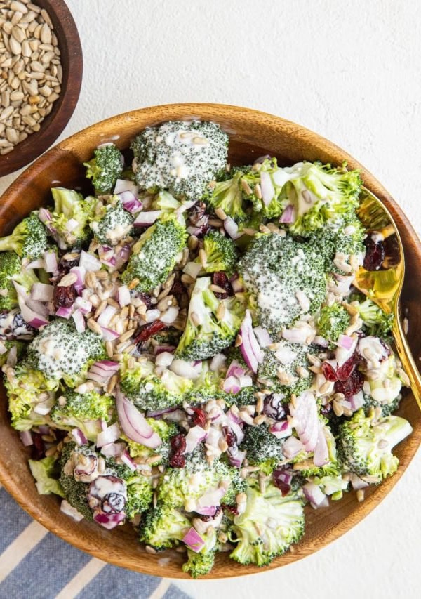 Wooden bowl full of broccoli salad with a striped napkin to the side and a bowl of sunflower seeds