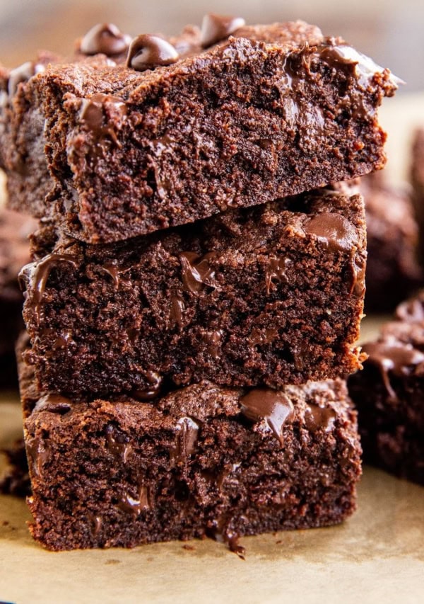 Stack of three coconut flour brownies with gooey chocolate shining through.