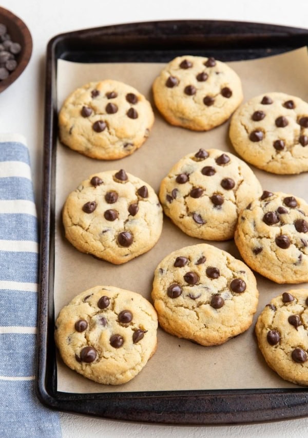 Coconut flour keto cookies on a baking sheet with a blue striped napkin to the side and a wooden bowl of chocolate chips