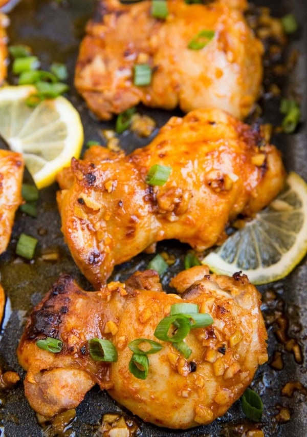 Casserole dish with baked boneless lemon garlic chicken thighs with sliced of lemon and green onion.