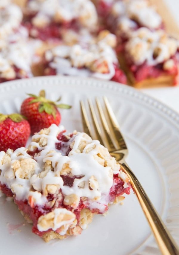 strawberry oatmeal bar on a plate with a gold fork and bars in the background