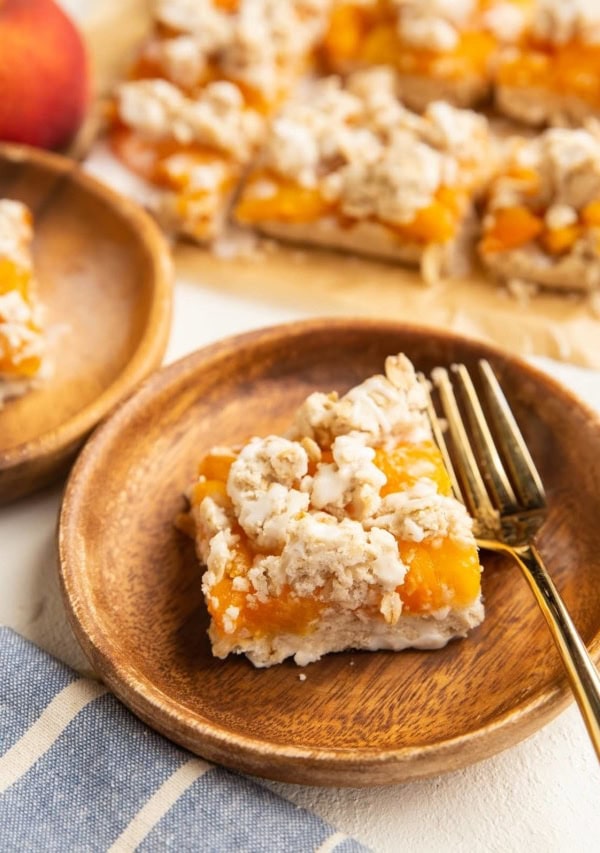 two wooden plates with slices of peach pie bars and more pie bars in the background