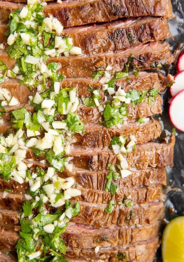 Carne Asada sliced on a black cutting board with garlic and cilantro on top