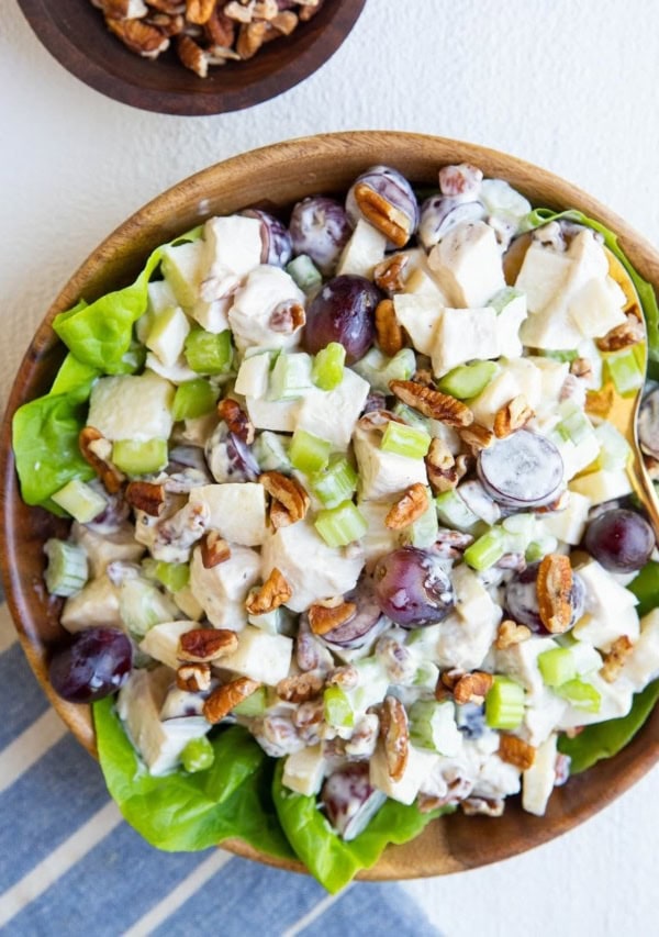 wooden bowl of chicken salad on a bed of butter lettuce with a blue striped napkin and a wooden bowl of pecans