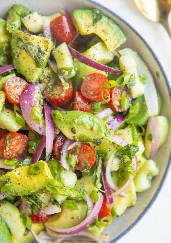 blue-rimmed bowl of avocado salad with a gold spoon to the side.