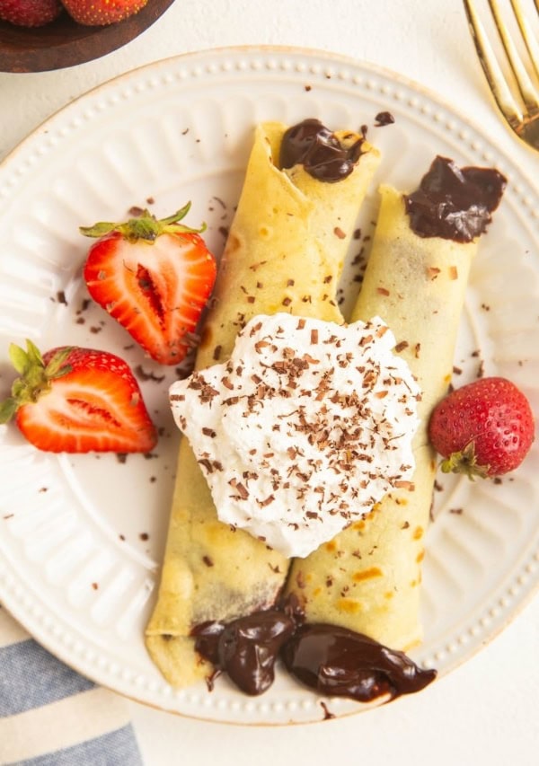 Plate of gluten-free crepes with chocolate filling, topped with whipped cream and berries.