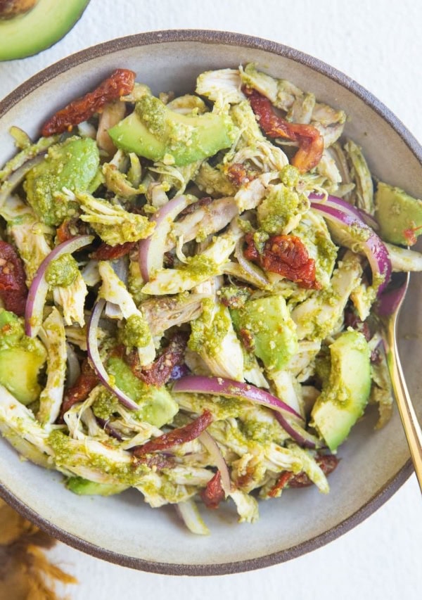 large bowl of pesto chicken salad with avocado, red onion and sun-dried tomatoes.