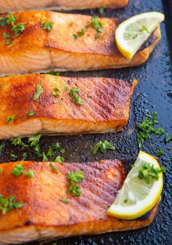 Baking dish with four salmon fillets fresh out of the oven with slices of lemon.