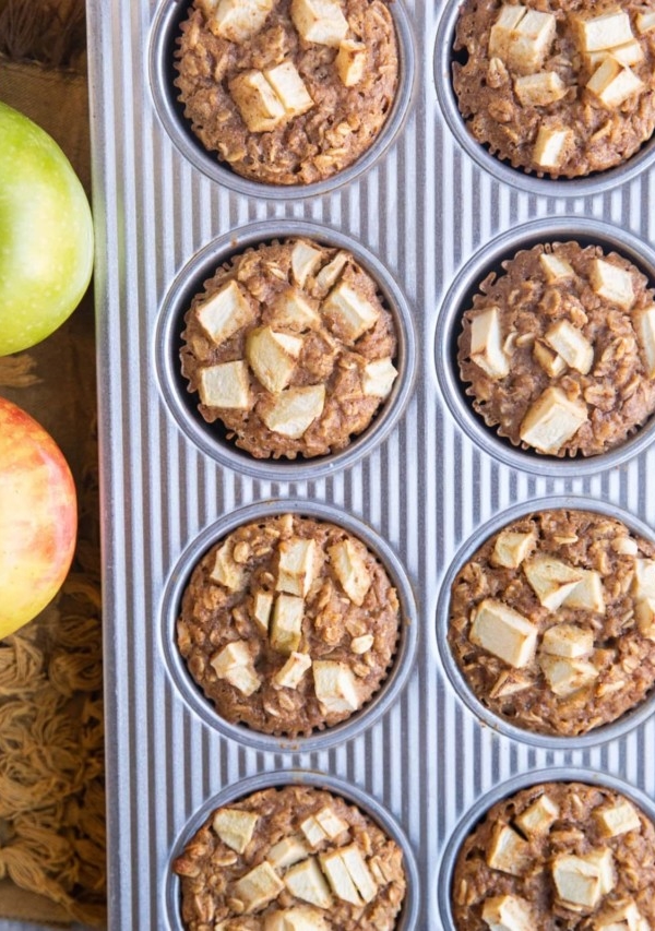 Muffin tray with finished oatmeal muffins and fresh apples to the side.