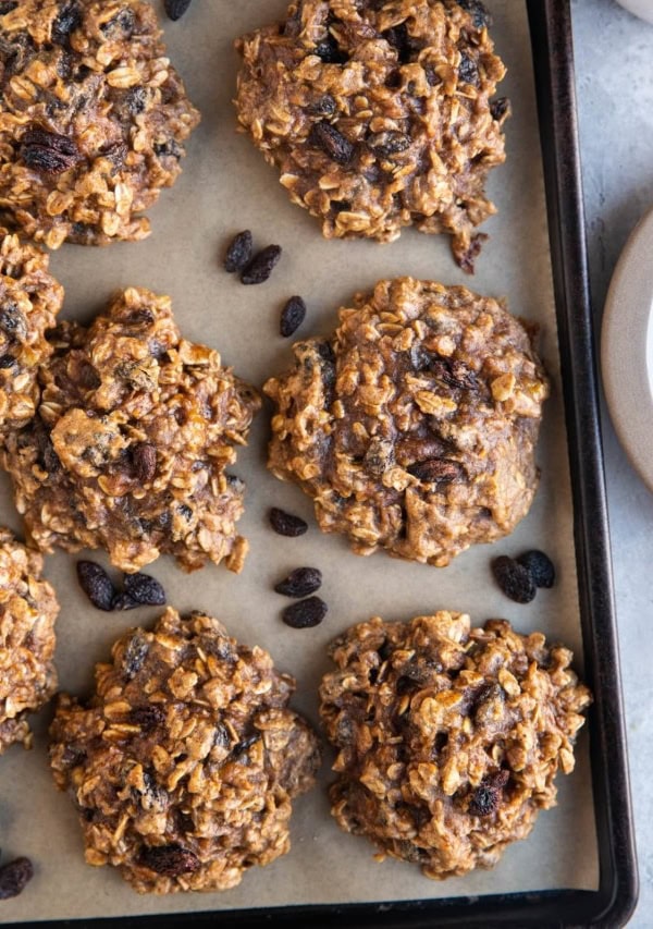 Top down photo of 6-Ingredient Healthy Oatmeal Raisin Cookies on a baking sheet with rogue raisins around the cookies