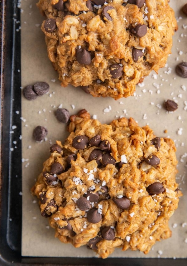 Baked peanut butter oatmeal cookies on a parchment lined baking sheet sprinkled with sea salt and extra chocolate chips.