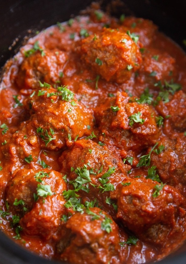 Angle shot of Italian meatballs in a crock pot, sprinkled with fresh parsley.