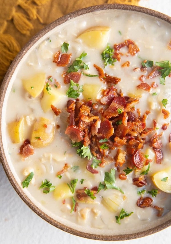 Close up top down photo of clam chowder in a bowl with crispy bacon and fresh parsley on top.