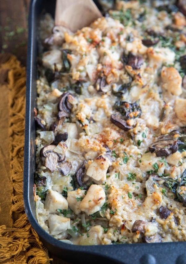 Large casserole dish full of chicken and mushroom casserole with creamy rice sitting on a rustic wood background. A wooden spoon in the casserole for serving.