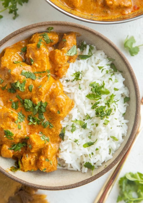 Close up top down image of bowl of chicken tikka masala and jasmine rice with chopped cilantro on top.