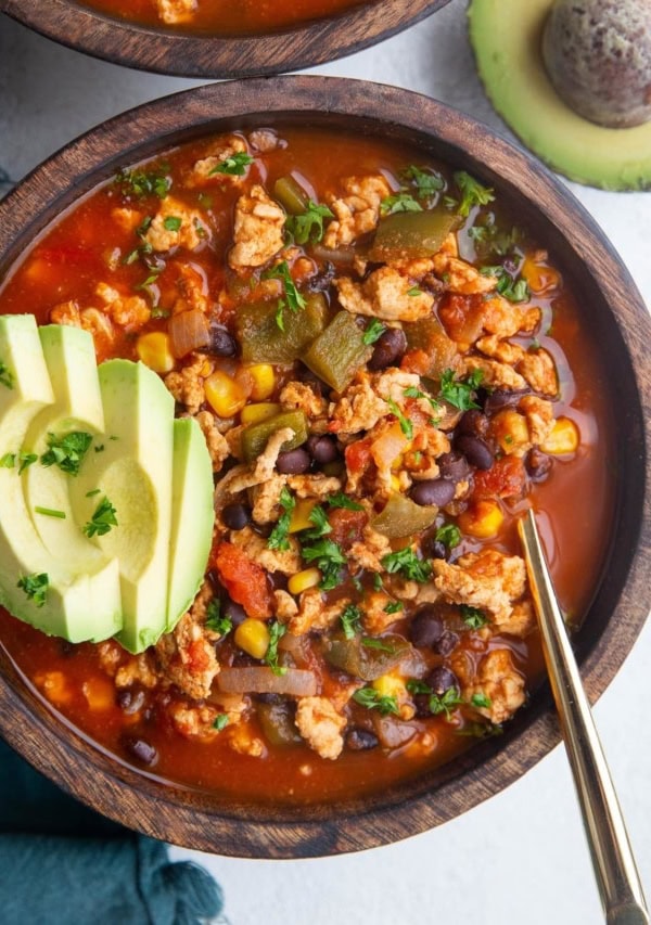 Two large wooden bowls of ground turkey taco soup with sliced avocado on top, ready to eat.