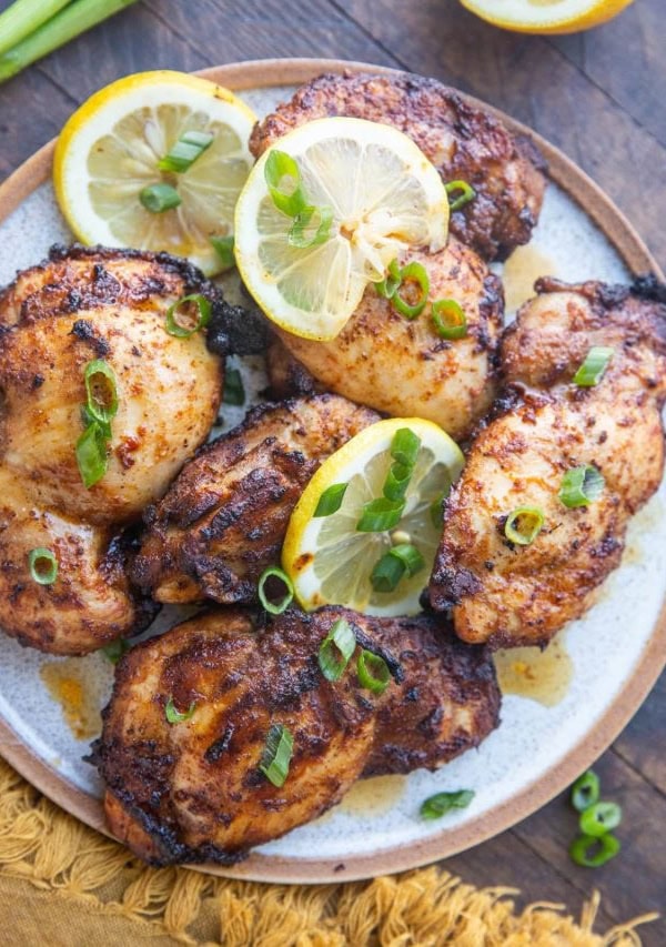 Top down plate of Mediterranean chicken sprinkled with green onions and slices of lemon on a rustic wooden background.