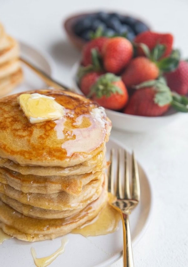 Angled shot of a stack of protein pancakes with syrup dripping down the side and butter on top.